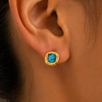 Paloma Cushion Stone Earrings – blue cushion-cut stud in a gold setting worn on an ear
