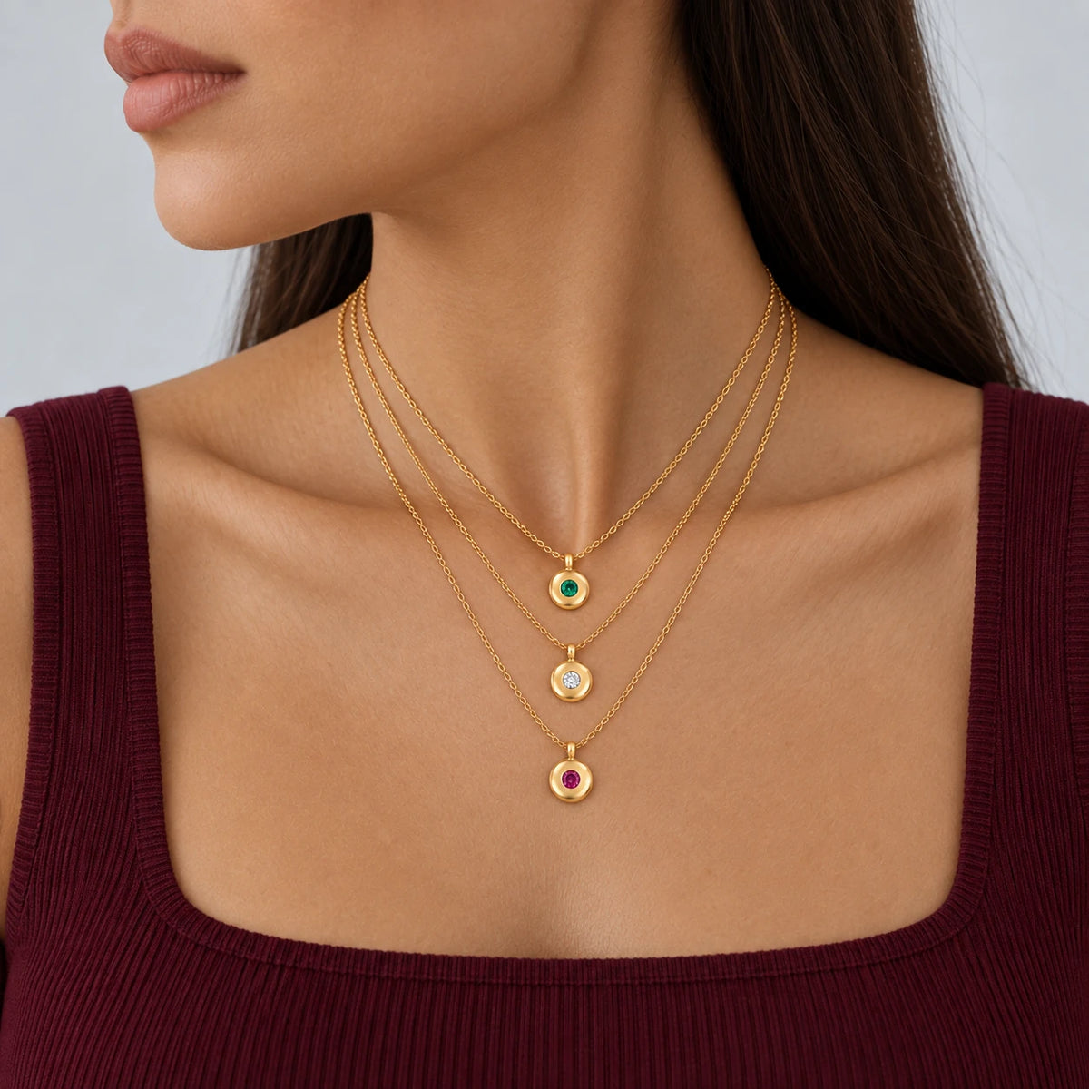 Model wearing three layered Ruth Birthstone Necklaces with green, clear and pink stones and a burgundy top