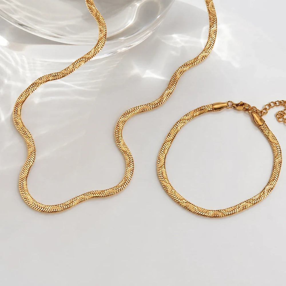 Serein Bracelet – gold herringbone bracelet beside a matching necklace and glass dish
